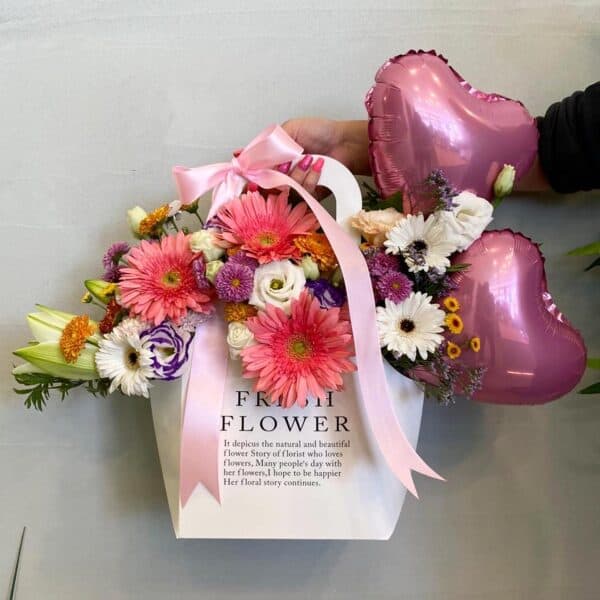 סל פרחים מיוחד מלא בפרחים ורודים סגולים ולבנים עם 2 בלוני לבבות.