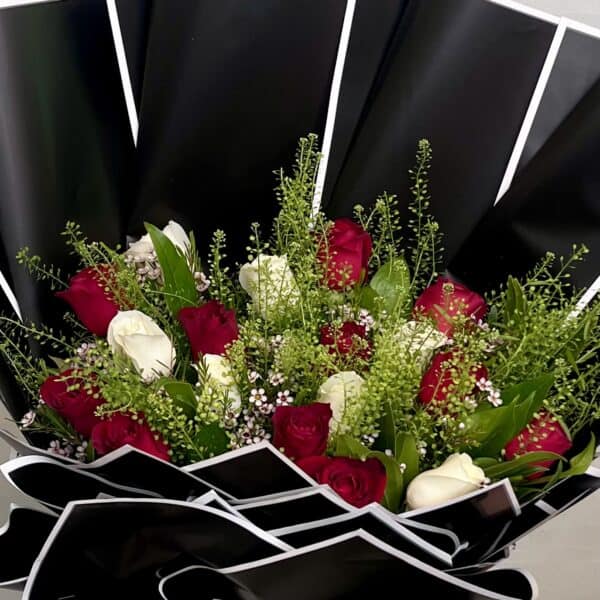 זר ורדים אדומים ולבנים בשילוב ירק וענפי קישוט. מעוצב בעטיפה מיוחד בצבע שחור עם מסגרת לבנה. צולם על רקע הקיר בחנות.