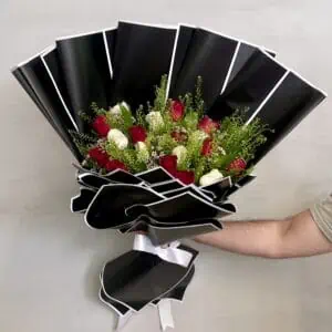 זר ורדים אדומים ולבנים בשילוב ירק וענפי קישוט. מעוצב בעטיפה מיוחד בצבע שחור עם מסגרת לבנה. צולם על רקע הקיר בחנות.