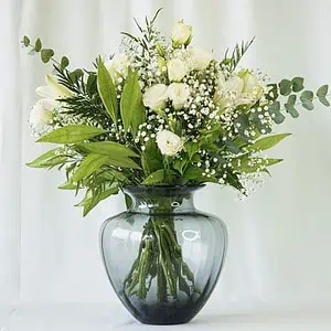 זר פרחים לבן שזור בתוך אגרטל מיוחד צבע כחול עמוק. הזר שזור מפרחי שושן צחור, ליזיאנטוס לבן, גיבסנית לבנה בשילוב ירק וענפי קישוט.